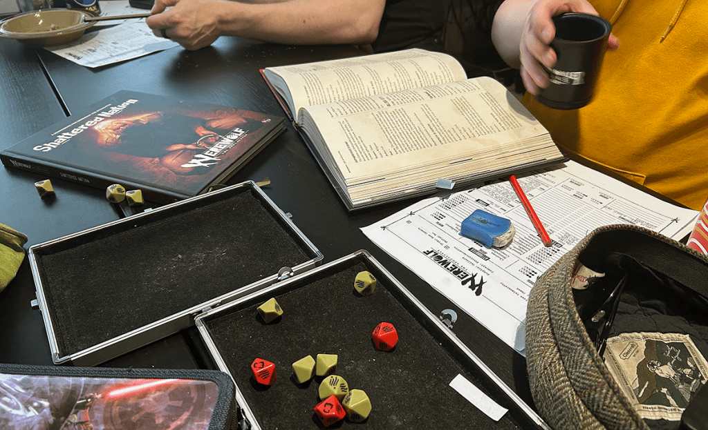 Cluttered gaming table with dice tray, dice, books, character sheets, etc.